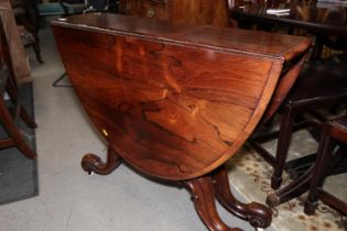 A 19th century rosewood oval drop leaf table, on folding quadruple scroll supports, 36" wide x 48"