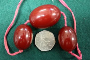 Three cherry amber Bakelite beads, the largest oval bead, 40mm long, on silk thread, 45.6g gross