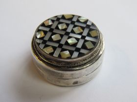 A white metal pill pot set with onyx and mother of pearl having Arabic hallmarks, 3.5cm dia.