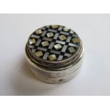 A white metal pill pot set with onyx and mother of pearl having Arabic hallmarks, 3.5cm dia.