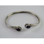 A silver and amethyst bangle, stamped 925 and having oval cabachon to each terminal.