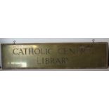 A large brass 'Catholic Central Library' sign mounted on wooden board, overall 95cm wide.