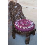 A contemporary carved Indo-Asian style low fireside chair having purple embroidery seat with fire