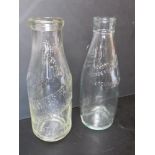 Two vintage clear glass milk bottles, one marked for Maynes Farm and Newbery Dairies St Albans.