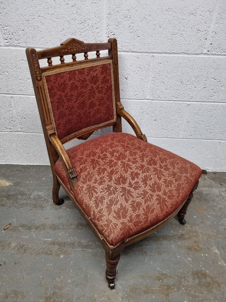 A low Edwardian fireside chair having been re-upholstered in red leaf pattern fabric having floral