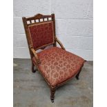 A low Edwardian fireside chair having been re-upholstered in red leaf pattern fabric having floral