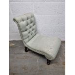 A low fireside chair upholstered in pale green fabric raised over brass and ceramic castors having