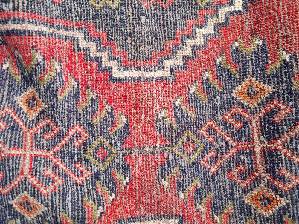 A 100% woollen rug in red ground having geometric pattern and measuring approx. 220 x 136cm. - Image 2 of 3