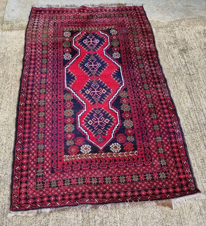 A 100% woollen rug in red ground having geometric pattern and measuring approx. 220 x 136cm.