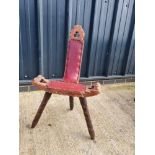 A carved wooden three legged high backed stool having leatherette seat.