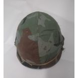 A 1980's US M1 helmet with liner and woodland camo cover.