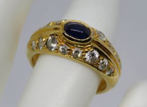 A yellow metal ring having central oval sapphire cabachon surrounded by white paste stones,