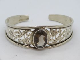 A pierced and engraved silver bangle having large smoky quarts oval cut stone to centre,
