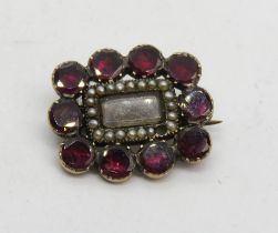 A Georgian mourning brooch having ten foil backed garnet stones around a glazed panel containing a