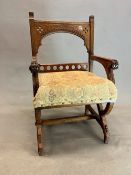 A NEOGOTHIC OAK ELBOW CHAIR, THE ARCHED TOP RAIL CARVED WITH A CHEVRON BAND ABOVE A STUFFED SEAT,