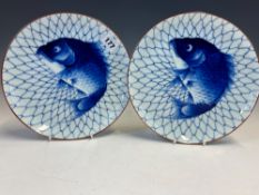 A PAIR OF JAPANESE ARITA BLUE AND WHITE PLATES, EACH PAINTED WITH A FISH CAUGHT AGAINST A NET