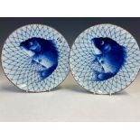 A PAIR OF JAPANESE ARITA BLUE AND WHITE PLATES, EACH PAINTED WITH A FISH CAUGHT AGAINST A NET