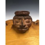 A TERRACOTTA MUG HAND MODELLED AS A HEAD OF A NATIVE SOUTH AMERICAN, HIS BRAIDED HAIR CROWNED BY A