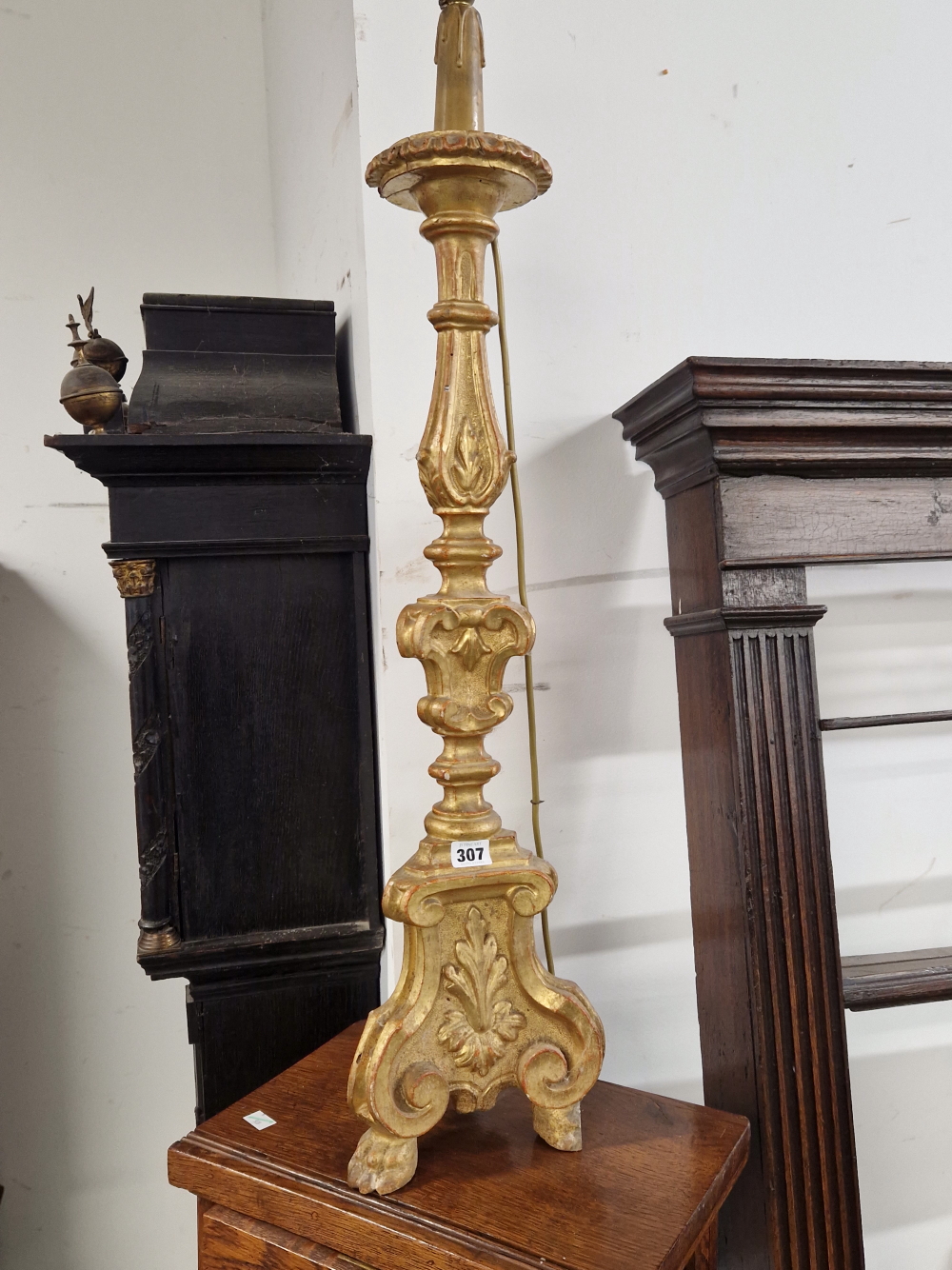 A BAROQUE STYLE GILT AND CARVED WOOD CANDLESTICK LAMP, THE BASE WITH THREE BRACKET LEGS CENTRED BY