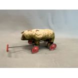 AN EARLY 20th C. FOUR WHEEL PULL ALONG BEAR, ITS VELVETEEN COVERED BODY FILLED WITH EXCELSIOR