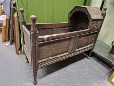 AN 18th/19th C. OAK CRADLE WITH A HOOD TO ONE END OF THE PANELLED SIDES ABOVE FOUR CYLINDRICAL