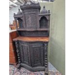 AN INDIAN HARDWOOD CABINET, THE RECESSED BOW FRONT DOOR TO THE TOP CARVED WITH A FLAUTIST AND