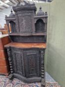 AN INDIAN HARDWOOD CABINET, THE RECESSED BOW FRONT DOOR TO THE TOP CARVED WITH A FLAUTIST AND