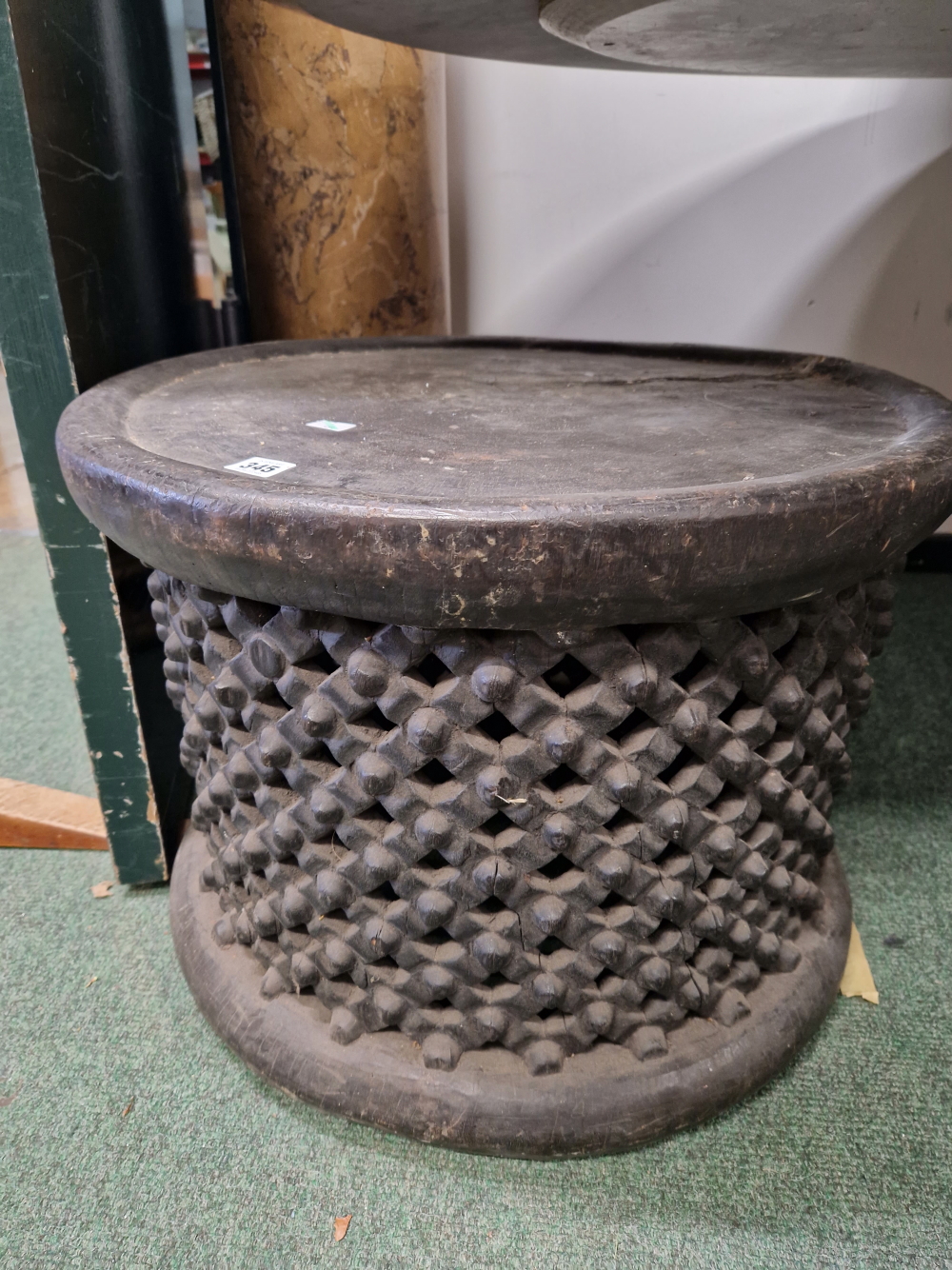 A BAMILEKE BLACK STOOL, THE DISHED CIRCULAR TOP ABOVE DIAMOND DIAPER PIERCED AND BOSS CENTRED SIDES.