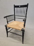 A WILLIAM MORRIS STYLE EBONISED ELBOW CHAIR WITH A RUSH SEAT