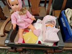 A PLASTIC DOLL WITH HAND KNITTED CLOTHES AND A SMALL CARRY COT WITH FURTHER CLOTHES