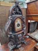 A MANTEL CLOCK IN AN OAK CASE CARVED WITH FOLIAGE ABOUT A CHILDS MASK BELOW THE SILVERED DIAL WITH