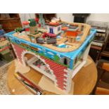A CHILDS PLAY TABLE BEARING A WOODEN RAILWAY, TRACK SIDE BUILDINGS AND SOME VEHICLES