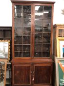 A LARGE REGENCY MAHOGANY GLAZED TOP BOOKCASE WITH PANEL DOOR BASE.