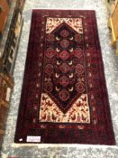 AN EASTERN HAND WOVEN RED GROUND SMALL CARPET 186 X 97CMS.