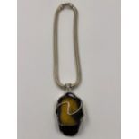 A LARGE PIECE OF AMBER IN A HALLMARKED SILVER SETTING SUSPENDED ON A LARGE SILVER SNAKE CHAIN. CHAIN