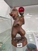 A BLACK FOREST WOODEN BEAR STANDING ON ITS HIND LEGS AND HOLDING UP A RED ORB