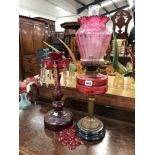 A VICTORIAN CRANBERRY GLASS OIL LAMP AND SHADE AND A SIMILAR CUT GLASSED LUSTER