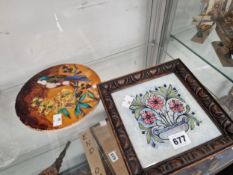 A CIRCULAR TILE SLIP DECORATED WITH A BIRD AND FLOWERS TOGETHER WITH A FRAMED FLORAL TILE