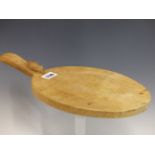 A ROBERT MOUSEMAN THOMPSON OAK OVAL CHEESE BOARD WITH A MOUSE CARVED TO ONE END OF THE HANDLE. W