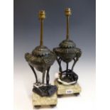 A PAIR OF TABLE LAMPS SUPPORTED ON URNS EACH WITH THREE RAMS HEADED LEGS AND ON SQUARE MOTTLED