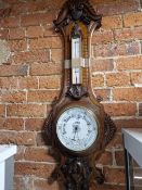 A VICTORIAN CARVED OAK CASED ANEROID BAROMETER WITH AN ALCOHOL THERMOMETER ABOVE THE WHITE CERAMIC