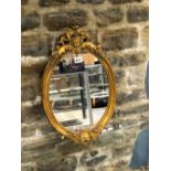 AN OVAL MIRROR WITHIN A GILT GESSO FRAME CRESTED BY A CHILDS HEAD AMONGST FLOWERS AND FOLIAGE. 52