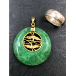 AN ORIENTAL GREEN HARDSTONE PENDANT TOGETHER WITH AN UNHALLMARKED SILVER BAND, FINGER SIZE J 1/2