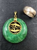 AN ORIENTAL GREEN HARDSTONE PENDANT TOGETHER WITH AN UNHALLMARKED SILVER BAND, FINGER SIZE J 1/2