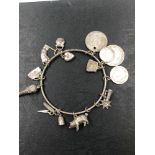 AN ANTIQUE SILVER BANGLE CHARM BRACELET, COMPLETE WITH VARIOUS SILVER CHARMS AND COINS. GROSS WEIGHT