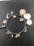 AN ANTIQUE SILVER BANGLE CHARM BRACELET, COMPLETE WITH VARIOUS SILVER CHARMS AND COINS. GROSS WEIGHT