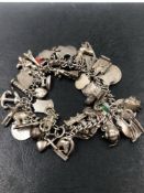 A VINTAGE CHARM BRACELET COMPLETE WITH A VARIED SELECTION OF SILVER AND WHITE METAL CHARMS AND
