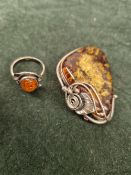 A SILVER AND AMBER ART NOUVEAU STYLE BROOCH/PENDANT AND A SIMILAR WHITE METAL AND AMBER RING