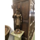 A PARCEL GILT IRON FIGURE OF A BEEFEATER SUPPORTING A SWORD POKER AND A FIRE BRUSH AT HIS BACK