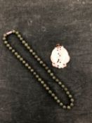 A ROW OF SPINACH GREEN JADE BEADS WITH A SCREW BARREL CLASP, LENGTH 42cms, TOGETHER WITH A CARVED